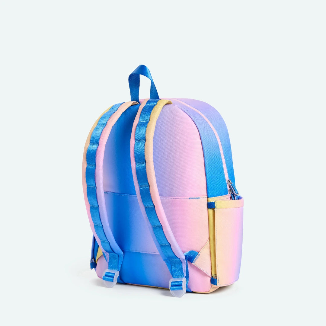Gradient backpack transitioning from blue to pink to yellow on a light purple background
