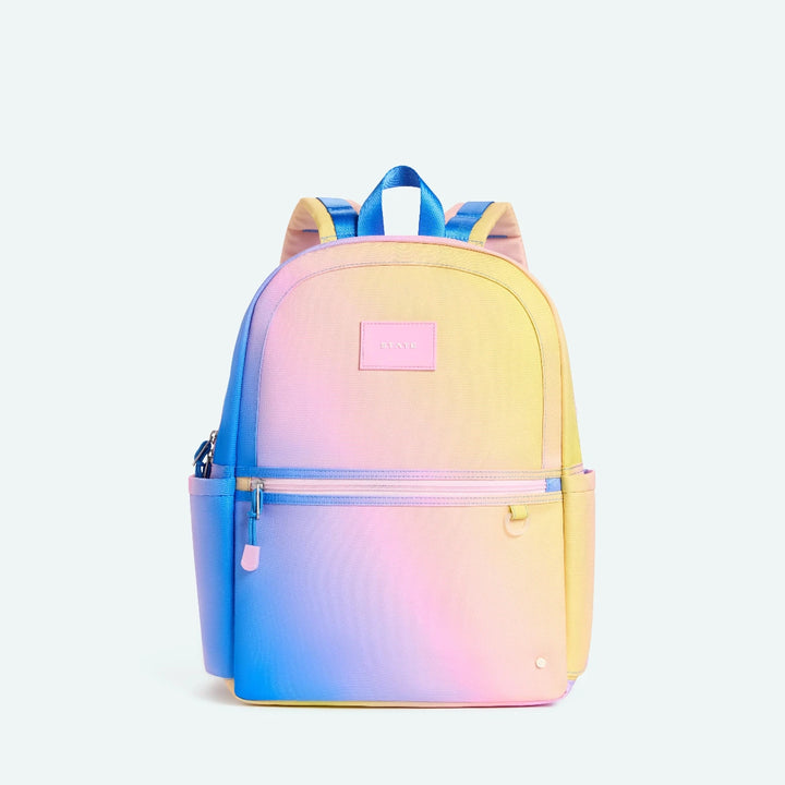 Gradient backpack transitioning from blue to pink to yellow on a light purple background