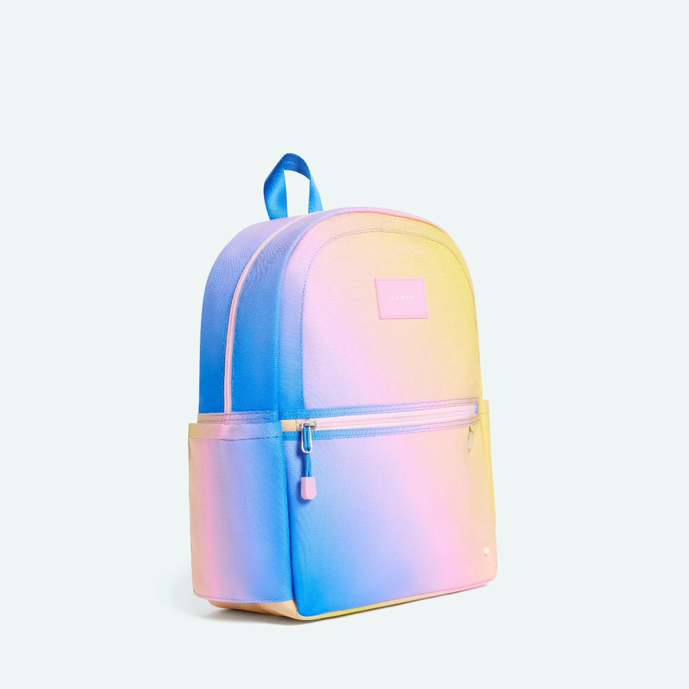Gradient backpack transitioning from blue to pink to yellow on a light purple background